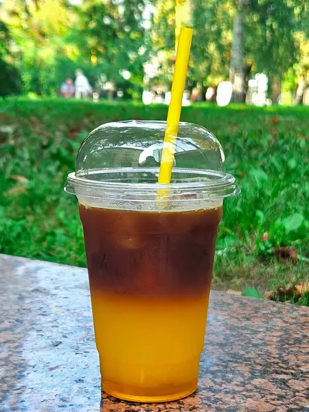 glass of cold drink with ice. Coffee with orange juice in a cafe outdoors. Summer drinks.Cold beverage in a plastic cup mockup