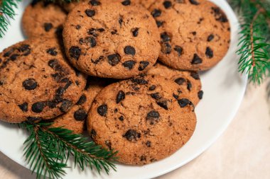 Tabakta çikolatalı kurabiyeler ve masada ladin dalları. Tabakta siyah çikolatalı kurabiyeler, Noel kurabiyeleri çikolatalı tarçınlı tatlı bayramı, yeni yıl yemeği ve Noel yemeği.