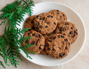 Tabakta çikolatalı kurabiyeler ve masada ladin dalları. Tabakta siyah çikolatalı kurabiyeler, Noel kurabiyeleri çikolatalı tarçınlı tatlı bayramı, yeni yıl yemeği ve Noel yemeği.