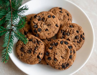 Tabakta çikolatalı kurabiyeler ve masada ladin dalları. Tabakta siyah çikolatalı kurabiyeler, Noel kurabiyeleri çikolatalı tarçınlı tatlı bayramı, yeni yıl yemeği ve Noel yemeği.