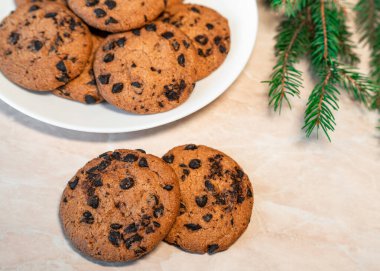 Tabakta çikolatalı kurabiyeler ve masada ladin dalları. Tabakta siyah çikolatalı kurabiyeler, Noel kurabiyeleri çikolatalı tarçınlı tatlı bayramı, yeni yıl yemeği ve Noel yemeği.