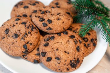 Tabakta çikolatalı kurabiyeler ve masada ladin dalları. Tabakta siyah çikolatalı kurabiyeler, Noel kurabiyeleri çikolatalı tarçınlı tatlı bayramı, yeni yıl yemeği ve Noel yemeği.
