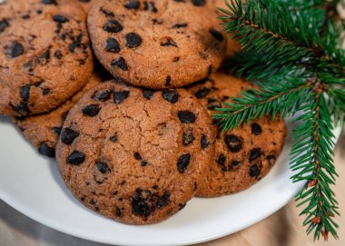 Tabakta çikolatalı kurabiyeler ve masada ladin dalları. Tabakta siyah çikolatalı kurabiyeler, Noel kurabiyeleri çikolatalı tarçınlı tatlı bayramı, yeni yıl yemeği ve Noel yemeği.
