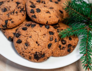 Tabakta çikolatalı kurabiyeler ve masada ladin dalları. Tabakta siyah çikolatalı kurabiyeler, Noel kurabiyeleri çikolatalı tarçınlı tatlı bayramı, yeni yıl yemeği ve Noel yemeği.