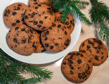 Tabakta çikolatalı kurabiyeler ve masada ladin dalları. Tabakta siyah çikolatalı kurabiyeler, Noel kurabiyeleri çikolatalı tarçınlı tatlı bayramı, yeni yıl yemeği ve Noel yemeği.
