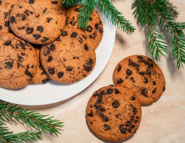 Tabakta çikolatalı kurabiyeler ve masada ladin dalları. Tabakta siyah çikolatalı kurabiyeler, Noel kurabiyeleri çikolatalı tarçınlı tatlı bayramı, yeni yıl yemeği ve Noel yemeği.