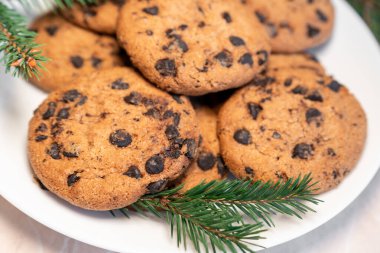 Tabakta çikolatalı kurabiyeler ve masada ladin dalları. Tabakta siyah çikolatalı kurabiyeler, Noel kurabiyeleri çikolatalı tarçınlı tatlı bayramı, yeni yıl yemeği ve Noel yemeği.