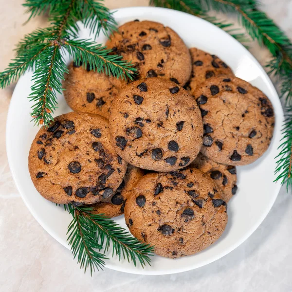 Chocolate cookies on a plate with spruce branches on the table. Dark chocolate cookies on a plate, Christmas cookies chocolate cinnamon sweet dessert holiday treat new year and christmas food on the table copy space food background