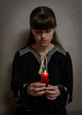 Karanlık bir arka planda yanan bir mumu olan genç bir kız. Elinde mum olan bir kız. Yanan bir muma bakan sevimli bir kızın portresi. Karanlık arka plan. Korkunç korku konsepti. Mumlu kadın.