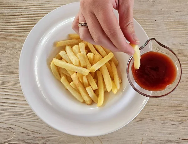 French fries and ketchup on a white plate. Hot golden french fries with sauce. Homemade rustic food.