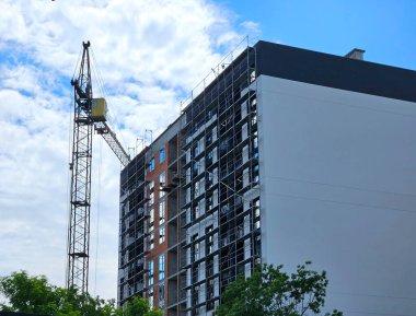 Mavi gökyüzüne karşı inşaat halindeki vinç ve bina. Çok katlı beton bir konut inşaatı