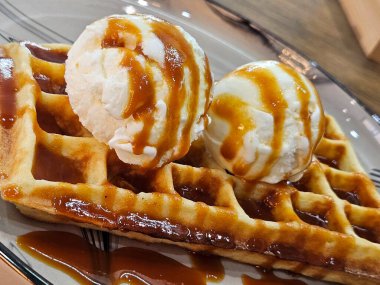 Dondurma ve şuruplu waffle. Karamelli Belçika waffle 'ına iki kepçe vanilyalı dondurma. Lezzetli waffle ve karamelli dondurma.