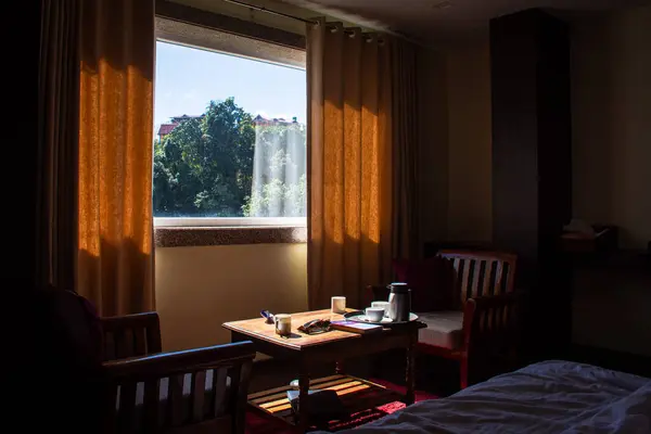 Güneş ışığı, ahşap mobilyaları ve açık hava manzarasını vurgulayarak, perdenin içinden sıcak bir iç kısma doğru akar. Sıcak ve davetkar bir atmosfer huzurlu bir dinlenme ve yansıma anında yakalanır.