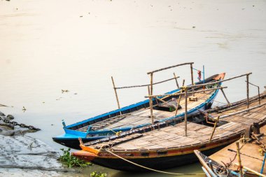 Bambu barınaklı ahşap kayıklar huzur ve doğal güzelliği yansıtan sakin bir nehir kıyısında dinleniyor..