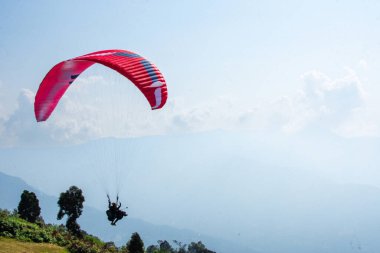 Renkli bir yamaç paraşütü gökyüzünde huzur içinde süzülüyor, nefes kesen bir dağ ve bulutlarla dolu bir arka plan, özgürlük ve macera hissi veriyor..
