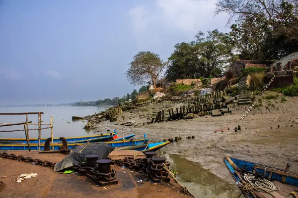 Çamurlu teknelerle dolu sakin bir nehir kıyısı, yıpranmış bir rıhtım, sudaki huzur ve tarihi tasvir ediyor..