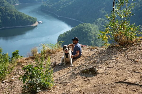 man and dog on mountain top overlooking a lake