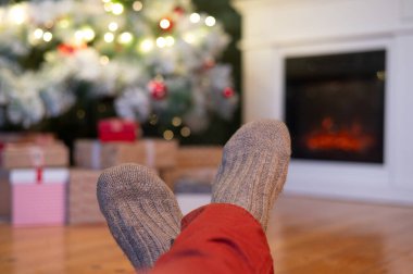 Ayaklar yün çoraplarda ve şömine arka planda Noel süslemeleri ile