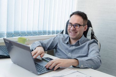 Modern mutfakta dizüstü bilgisayarda çalışan gülümseyen genç adam, sabah e-postaları kontrol eden, sosyal ağda mesaj yazan, interneti kullanan mutlu erkek, bilgi arayan