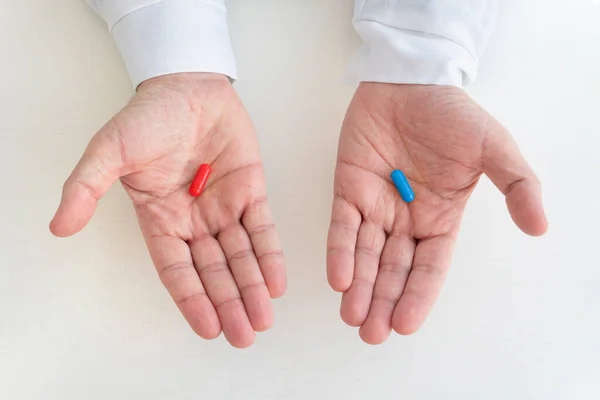 Hand taking medicine capsule pills on white background. a red and blue pill in a man\'s hand. The concept of choosing treatment and medicine.