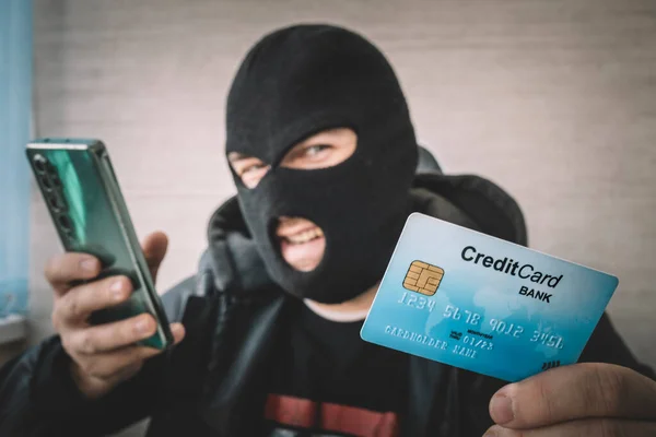 Close Man Robbery Mask Hood Holding Credit Card Looking Smartphone — Stock Photo, Image