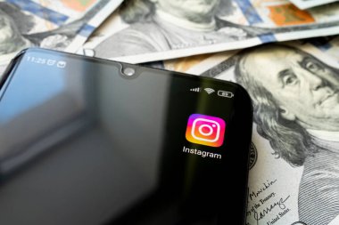 Instagram uygulamalı akıllı telefon ekranı ve bir sürü yüz dolarlık banknot. İş ve sosyal ağ kavramı. cep telefonunun siyah ekranındaki uygulama simgesi.