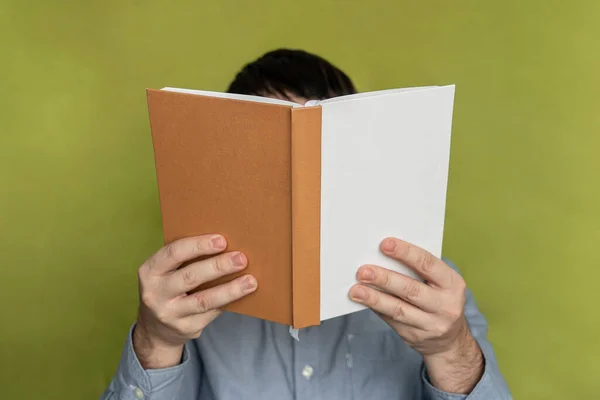 一个男人正在阅读一本绿色背景的白色和棕色封面的书 一个学生拿着一本有空封皮的课本 — 图库照片