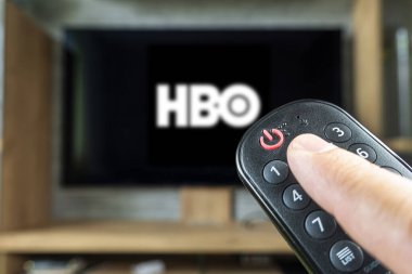 Barnaul. Rusya 20 Haziran 2022: Uzaktan kumanda elinde ve televizyon ekranında ABD kanalı HBO 'nun logosu. kapatma düğmesine odaklan