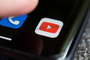 A smartphone lying on a table in the dark, displaying the logo of the YouTube. The finger above touch screen. Barnaul. Russia June 20, 2022 clipart