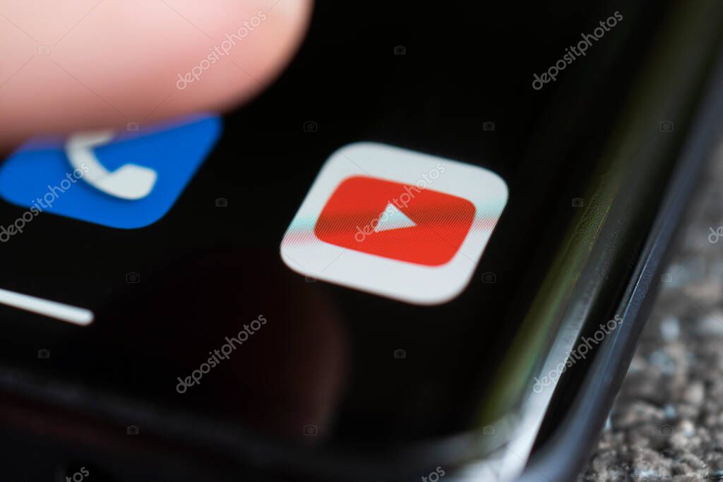 A smartphone lying on a table in the dark, displaying the logo of the YouTube. The finger above touch screen. Barnaul. Russia June 20, 2022