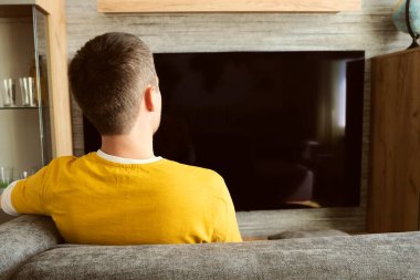Adam evde geniş ekran televizyon izliyor. Siyah bir TV ekranına karşı sarı tişörtlü bir izleyici.