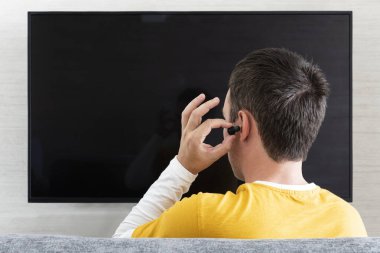 Bir adam kulağına kulaklığı TV ekranının arka planına dayayıp geceleri kulaklıkla televizyon izliyor..