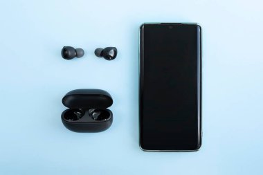 Akıllı telefon, kablosuz kulaklık ya da parlak mavi arka planda şarj çantası olan kulaklık. Müzik teknolojisi trendleri. en üstteki görünüm