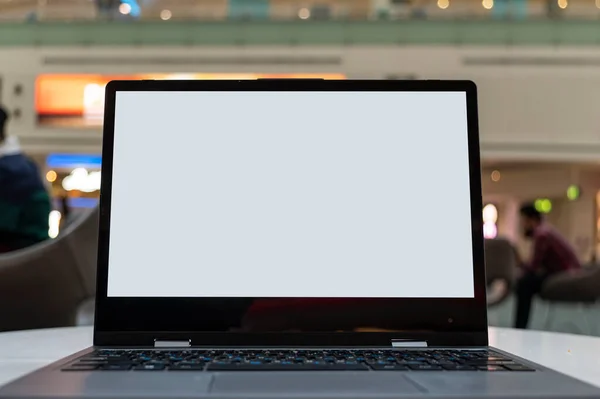 画像をモックアップ カフェやコーヒーショップ内の机の上に空白の白い画面のラップトップコンピュータの中に座っている人々のぼやけた背景を持つ カフェから働く コピースペース — ストック写真