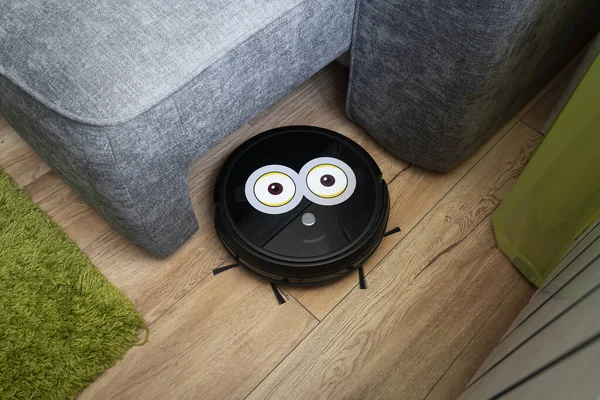 Automatic robot vacuum cleaner in black on a wooden floor . New modern technologies for apartment cleaning. smart home electronic assistant. robot vacuum cleaner goes around the sofa. home assistant