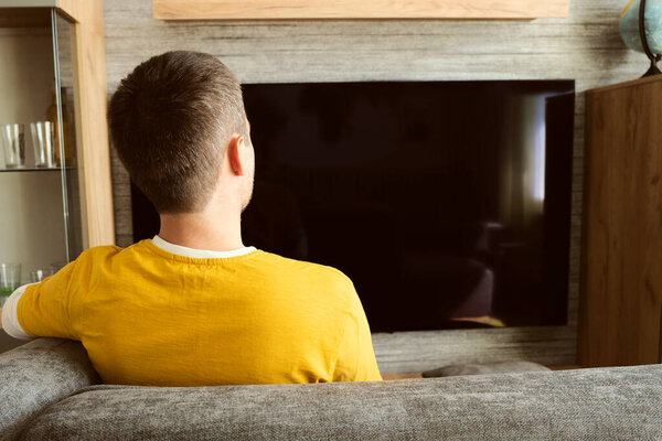 Man Watching Widescreen TV At Home. viewer in a yellow T-shirt against a black TV screen.