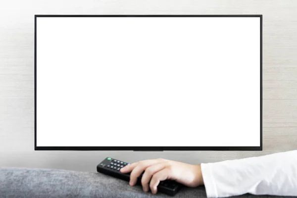 TV remote control in male hand in front of widescreen TV set with blank screen on white wall background. guy switches channels on the remote from the TV.