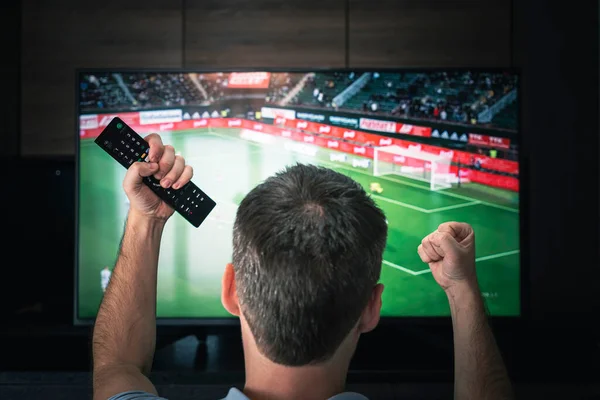 レジャー テクノロジー スポーツ エンターテイメント の概念 サッカーを見てリモート コントロールまたは自宅でテレビでサッカー ゲームを持つ男 テレビで試合を見て興奮しているサッカーファン — ストック写真