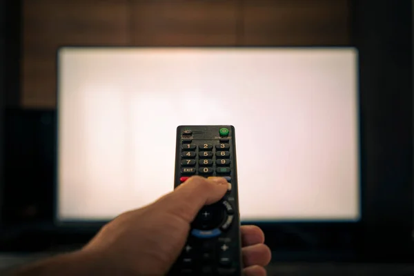 stock image blurred remote control for television. a man's hand holds the remote control in front of a large white TV screen.