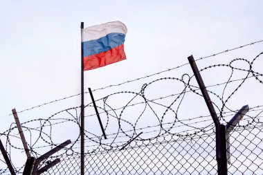 Rus bayrağının bulutlu gökyüzüne karşı dikenli tellerin arkasındaki görüntüsü. Rus karşıtı yaptırımlar. Rusya sınırında bir sınır karakolu. Rusya 'nın dünyadaki kültürünü iptal et