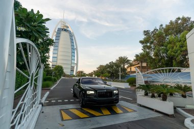 Kara rulo Royce, Dubai 'deki Burj Al Arap Oteli' nden akşam saatlerinde bulutlu güzel bir gökyüzünün arka planına doğru yola çıkıyor. Dubai, BAE, Birleşik Arap Emirlikleri. 27 Kasım 2022.