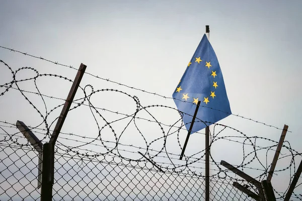 View of European union flag behind barbed wire against cloudy sky. Concept anti-Russian sanctions. border post on border of Russia. cancel culture Russia in world. ban on entry for Russians to Europe