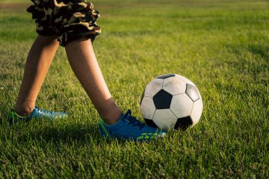 Klasik siyah-beyaz futbol topu ve yeşil çimlerin üzerindeki bir futbolcunun bacakları. Futbol maçı, antrenman, hobi konsepti. Fotokopi alanı. Genç bir çocuk topa vuruyor..