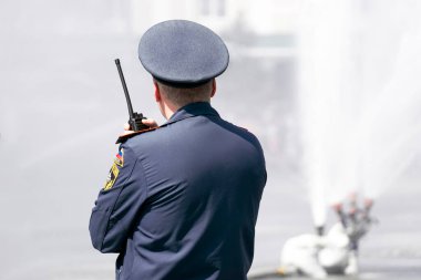 Üniformalı tanınmayan bir polis memuru şehirdeki çeşmenin oradaki sokakta bir telsizle konuşuyor. 1 Mayıs 2022 Barnaul Rusya
