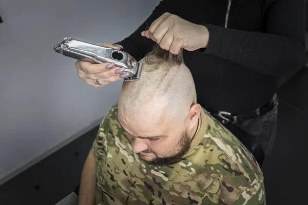 軍の制服を着た若い男が軍務のために頭をはげている 髭を生やした男が理容室で散髪してる — ストック写真
