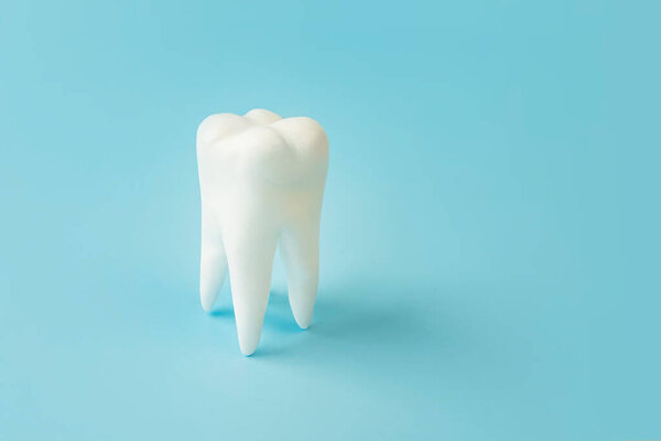 White healthy tooth on blue background with copy space.