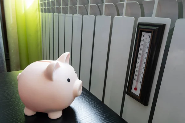 Piggy bank, thermometer near radiator. Saving heating in winter. price heating. Energy crisis, energy efficiency and rising heating costs in Europe