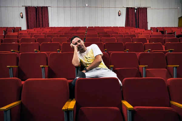 young man with glasses sleeping alone in cinema hall while everyone is gone. A lonely man in an empty theater fell asleep at the performance. An uninteresting boring opera.