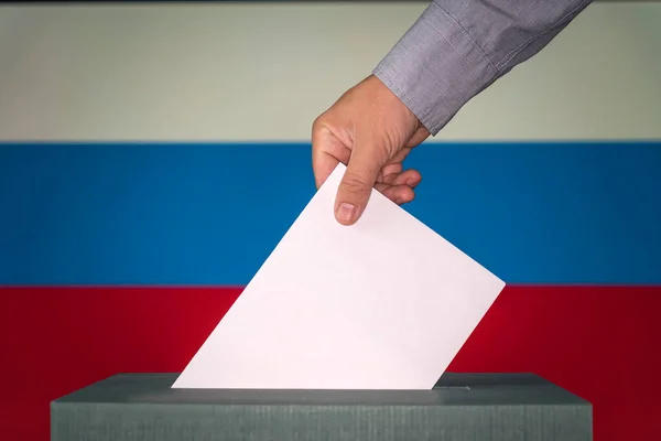ロシアは選挙の象徴です 男性の手は ロシアの旗の背景に投票用紙のシンボルとしてマークと紙の白いシートを置きます — ストック写真