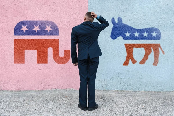 man thinks in the background wall with symbols of US parties. In American politics US parties are represented by either the democrat donkey or republican elephant. August 24, 2022